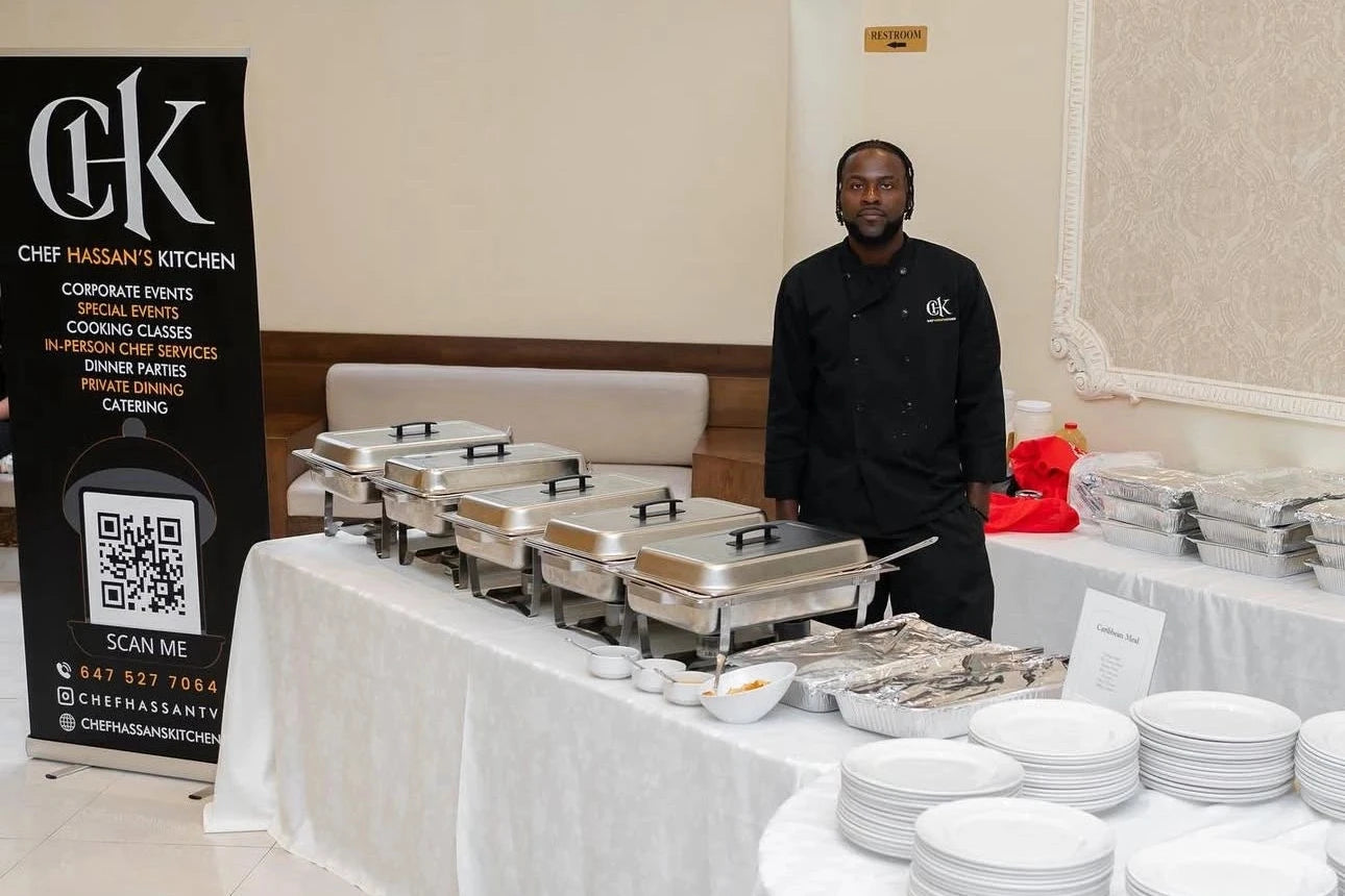 Man standing behind a buffet table with Chef Hasan's Kitchen branding in the background.