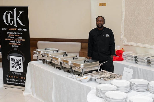 Man standing behind a buffet table with Chef Hasan's Kitchen branding in the background.