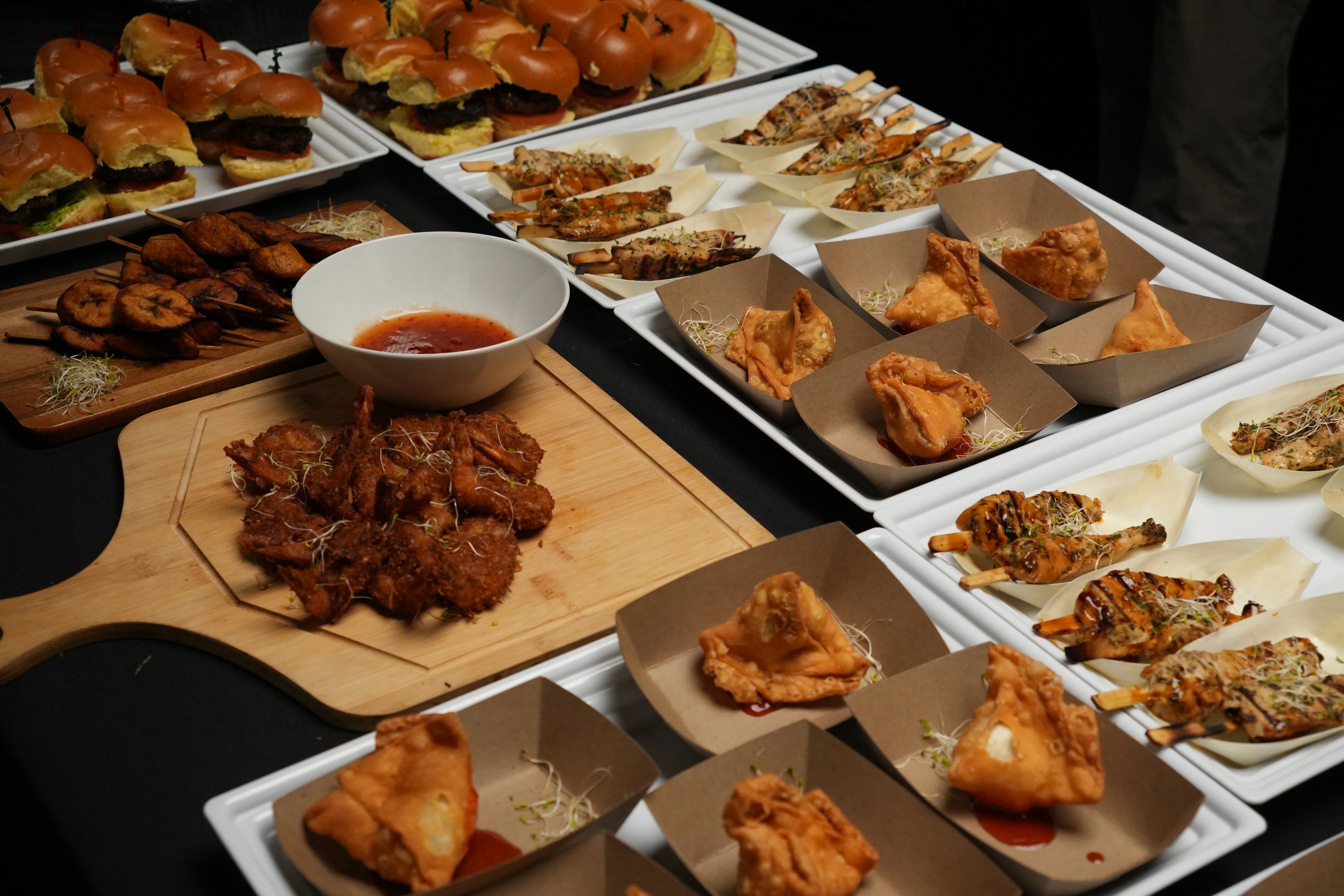 Assorted small plates of chef hassan dishes including fried items and a bowl of dipping sauce on a wooden board.