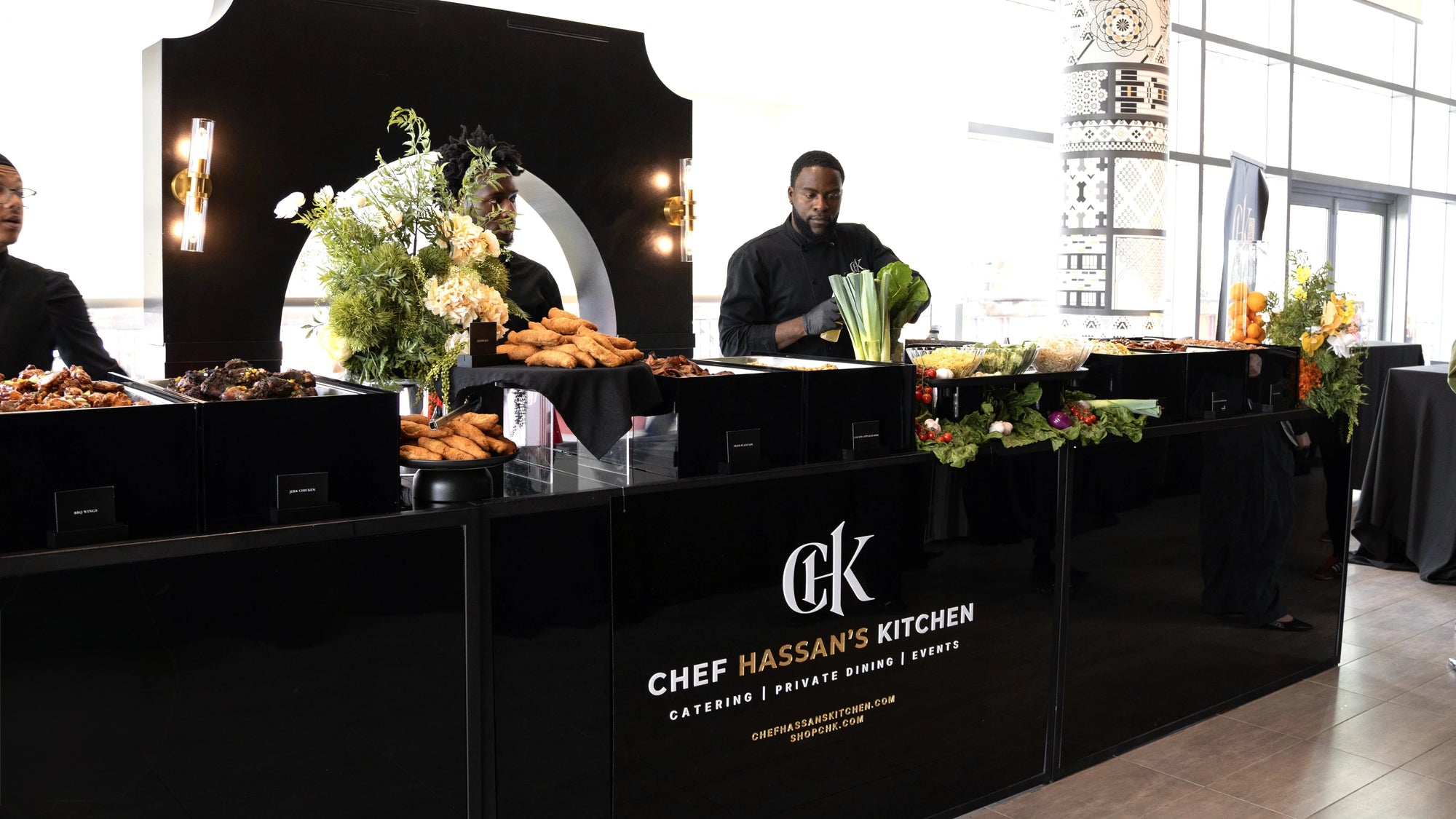 Buffet setup with food and 'Chef Hassan's Kitchen' branding in a modern interior.